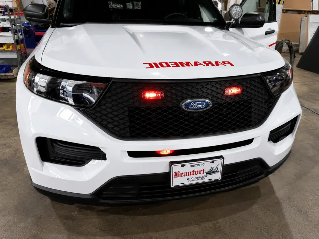Front view of a white Ford police SUV equipped with emergency warning lights, push bumper lighting, and law enforcement upfitting features inside a vehicle customization and fleet upfitting facility.