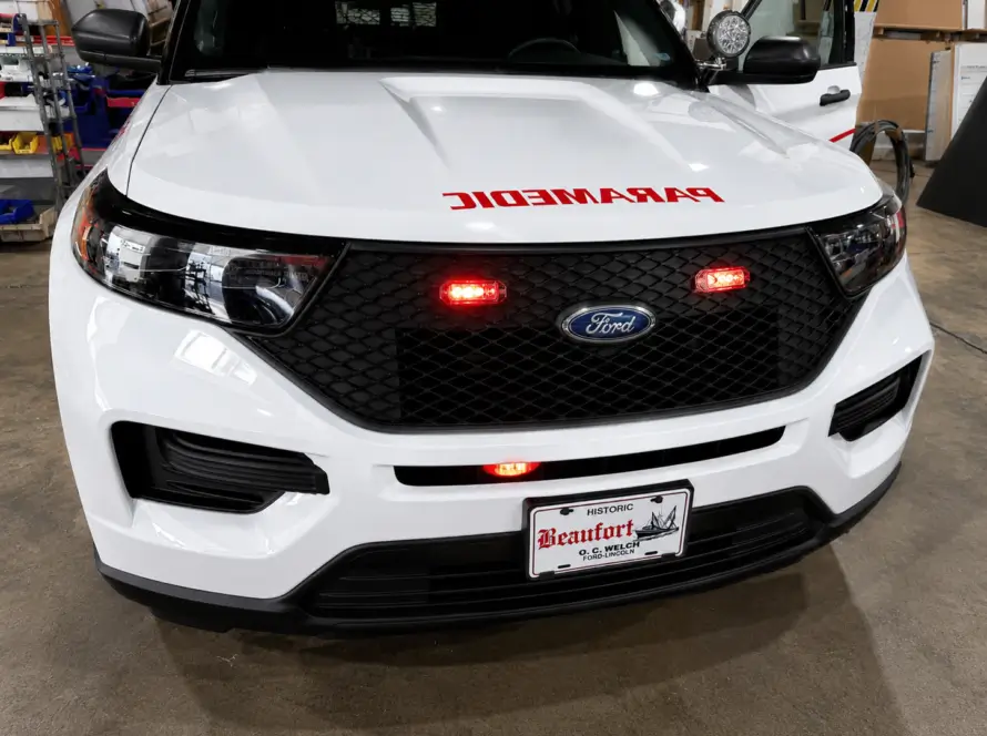 Front view of a white Ford police SUV equipped with emergency warning lights, push bumper lighting, and law enforcement upfitting features inside a vehicle customization and fleet upfitting facility.