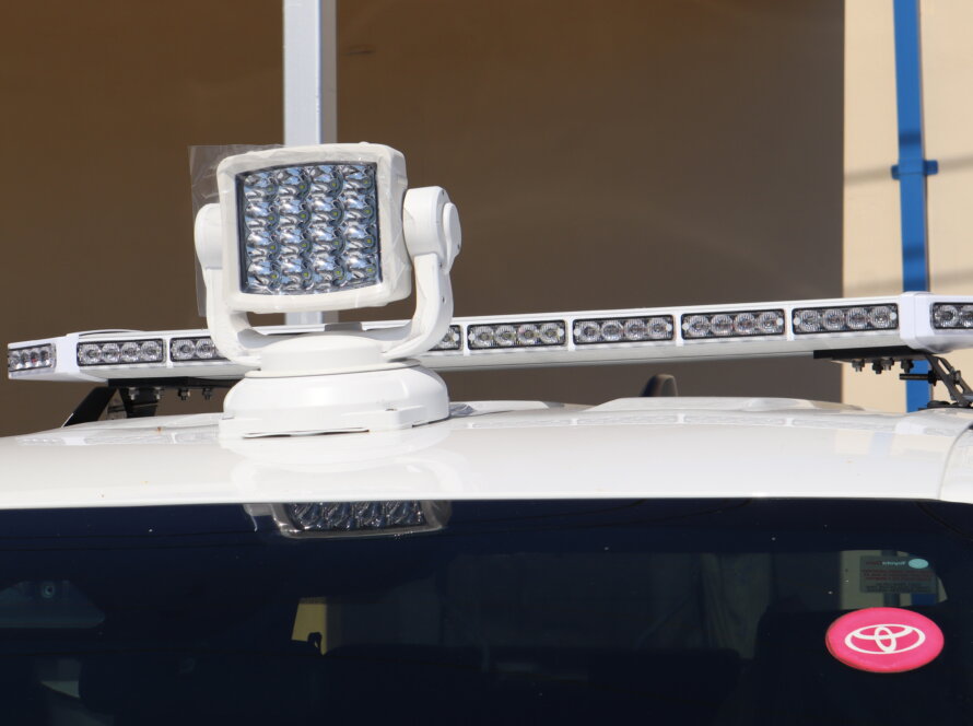 Close-up of a white utility vehicle equipped with a roof-mounted LED warning light bar and remote-controlled spotlight, designed for fleet, public works, emergency response, and roadside safety operations.