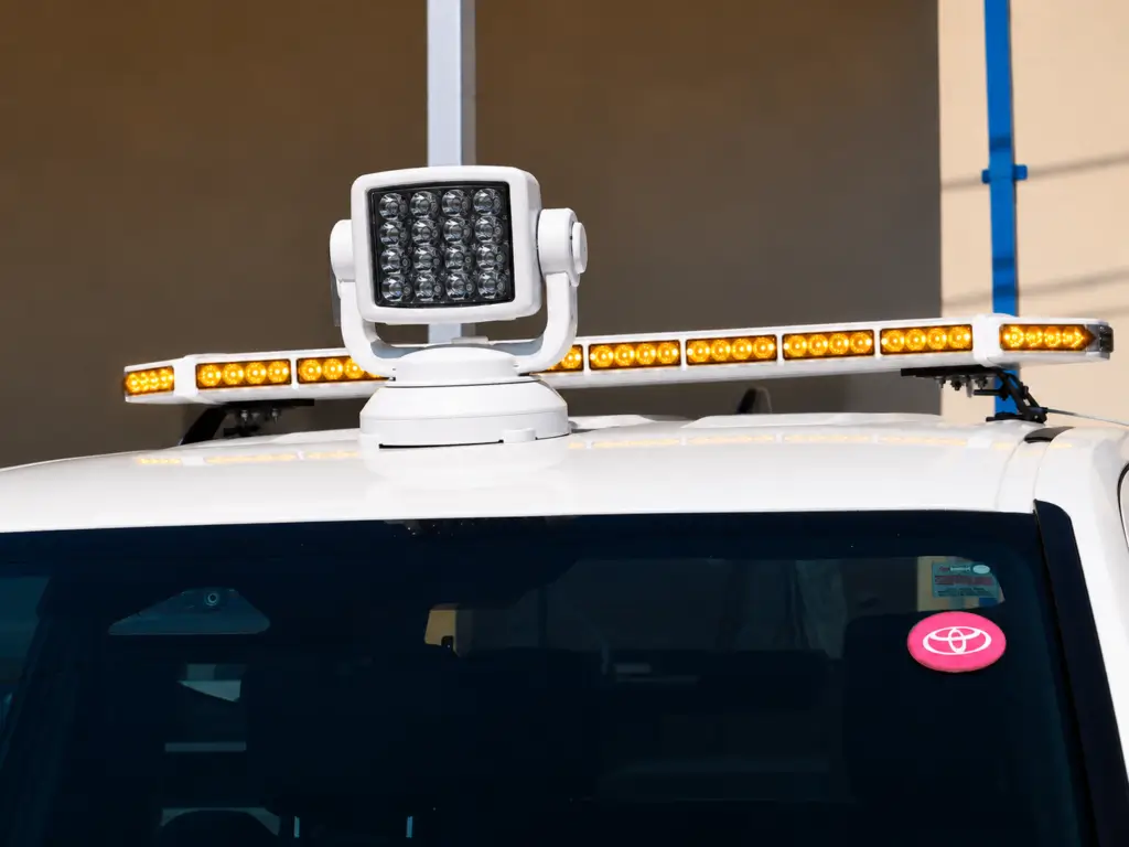 Close-up of an LED traffic advisor and directional warning bar mounted on a utility vehicle, featuring flashing amber lights and a roof-mounted work light designed to improve roadside visibility and traffic control safety.