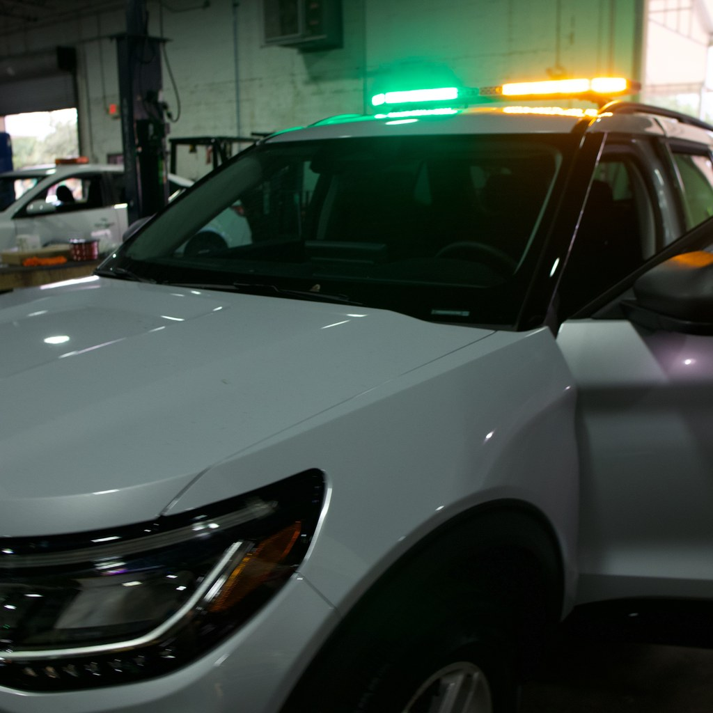White patrol Explorer with a green and amber LED light bar running in the OCM Upfitting shop